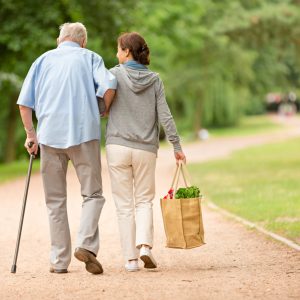 Nuorempi nainen antaa tukea iäkkäälle miehelle kävelyllä hoivapalvelun aikana